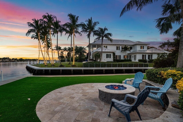 patio terrace at dusk with a yard, a water view, and a fire pit