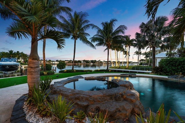 pool at dusk with a water view and an in ground hot tub