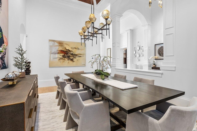 dining space with ornate columns, light hardwood / wood-style flooring, crown molding, a towering ceiling, and a chandelier