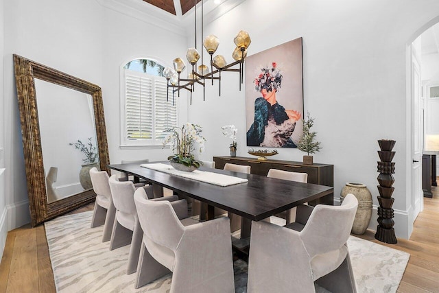 dining space with crown molding, a towering ceiling, a chandelier, and light wood-type flooring