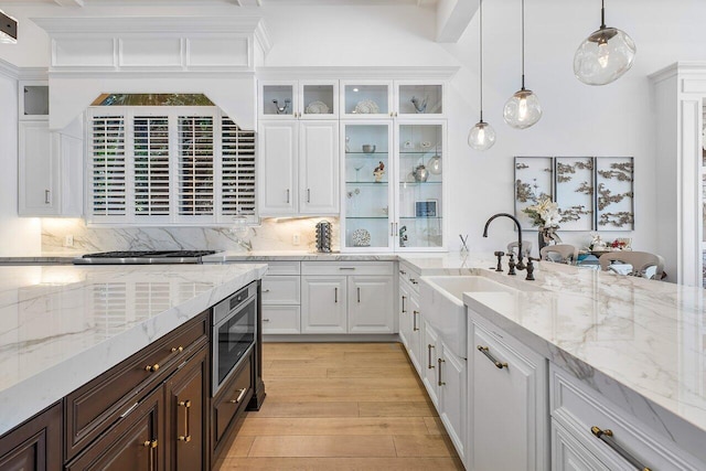 kitchen featuring stainless steel microwave, backsplash, light wood-type flooring, decorative light fixtures, and white cabinetry