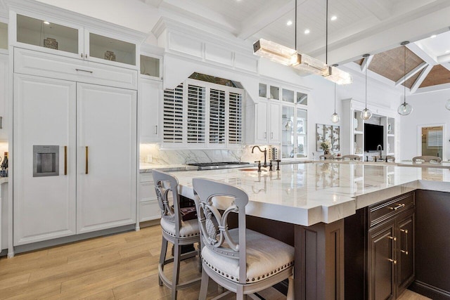 kitchen featuring an island with sink, pendant lighting, light hardwood / wood-style floors, a breakfast bar, and white cabinets