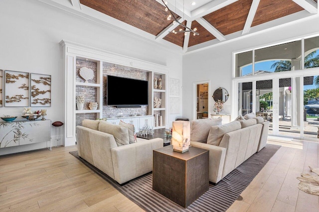 living room with built in shelves, an inviting chandelier, beamed ceiling, a towering ceiling, and light hardwood / wood-style floors