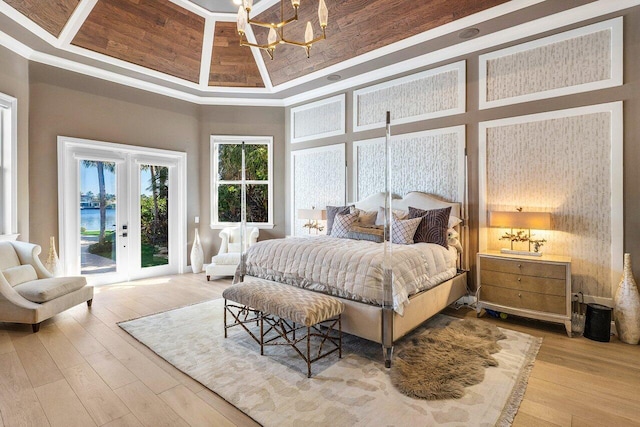 bedroom featuring a towering ceiling, access to outside, a raised ceiling, hardwood / wood-style flooring, and a chandelier