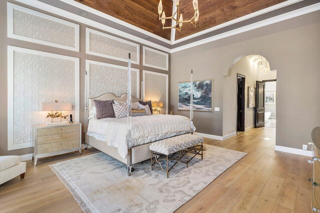 bedroom with a towering ceiling, a raised ceiling, crown molding, an inviting chandelier, and light hardwood / wood-style floors