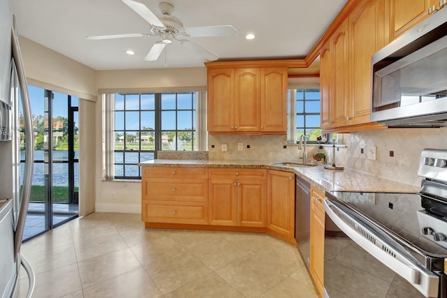 kitchen featuring backsplash, a water view, sink, light stone counters, and stainless steel appliances