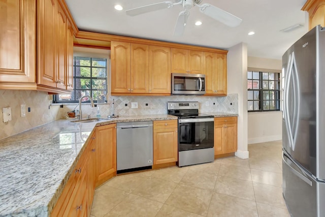 kitchen with light stone countertops, appliances with stainless steel finishes, backsplash, ceiling fan, and sink