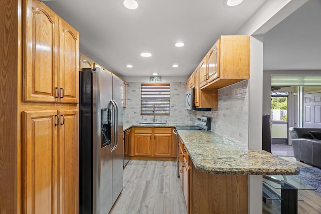 kitchen featuring sink, light stone counters, backsplash, light hardwood / wood-style floors, and appliances with stainless steel finishes