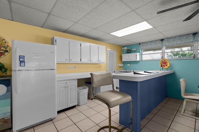 kitchen with a breakfast bar, light tile patterned flooring, white cabinets, ceiling fan, and white fridge