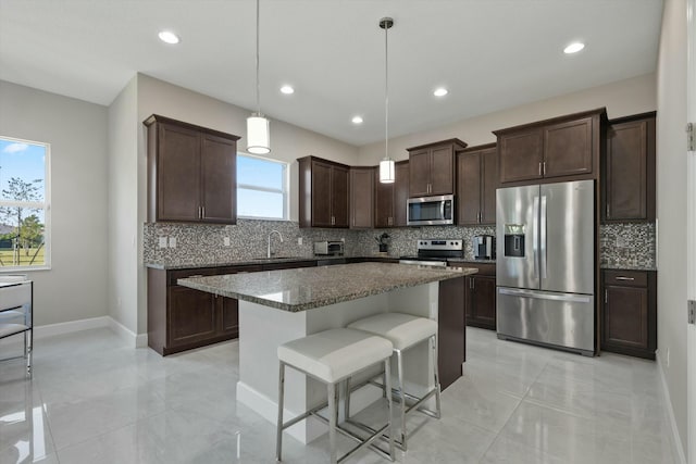 kitchen with dark brown cabinetry, decorative light fixtures, a breakfast bar area, a kitchen island, and appliances with stainless steel finishes