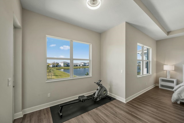 exercise room featuring dark hardwood / wood-style flooring, a water view, and plenty of natural light