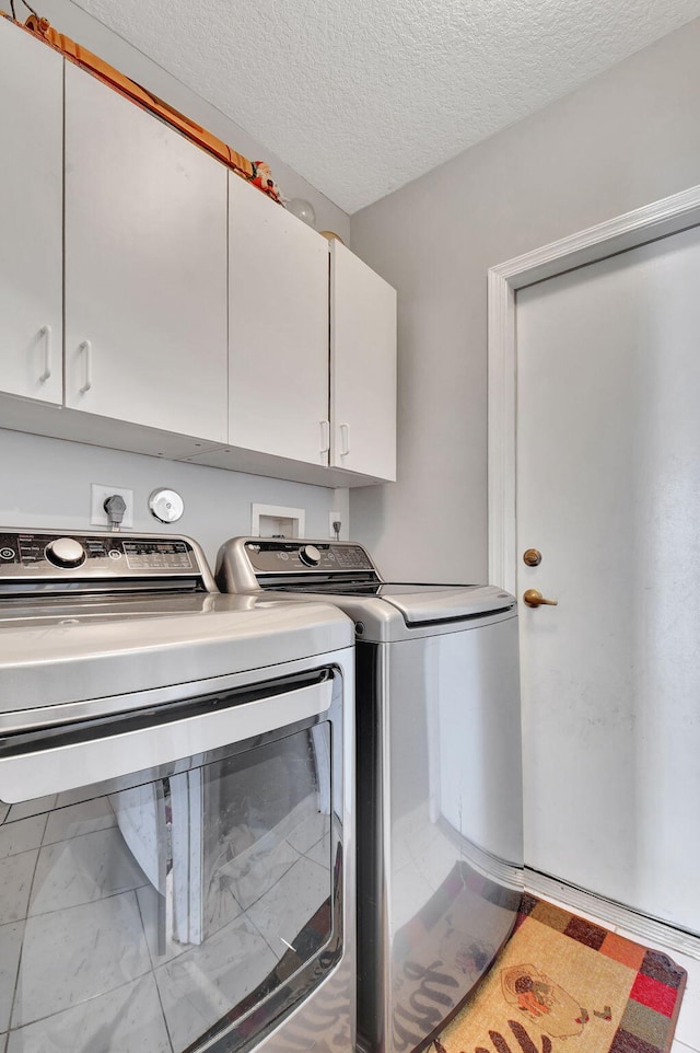 clothes washing area featuring washing machine and dryer, cabinets, and a textured ceiling