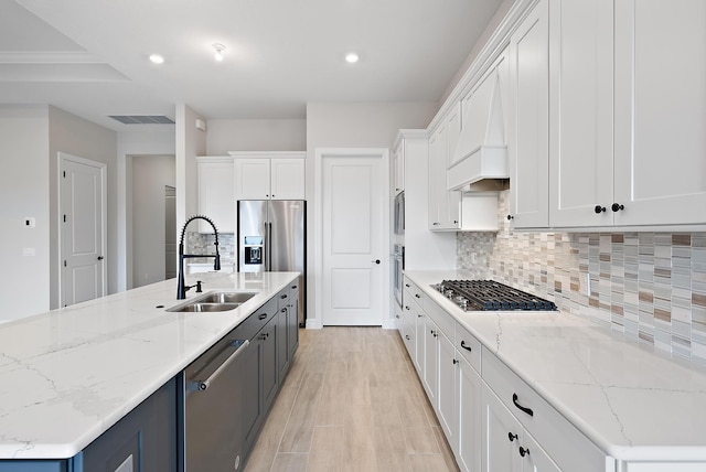 kitchen featuring light stone countertops, white cabinetry, sink, stainless steel appliances, and a kitchen island with sink