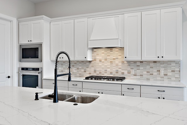 kitchen featuring decorative backsplash, appliances with stainless steel finishes, custom exhaust hood, sink, and white cabinets