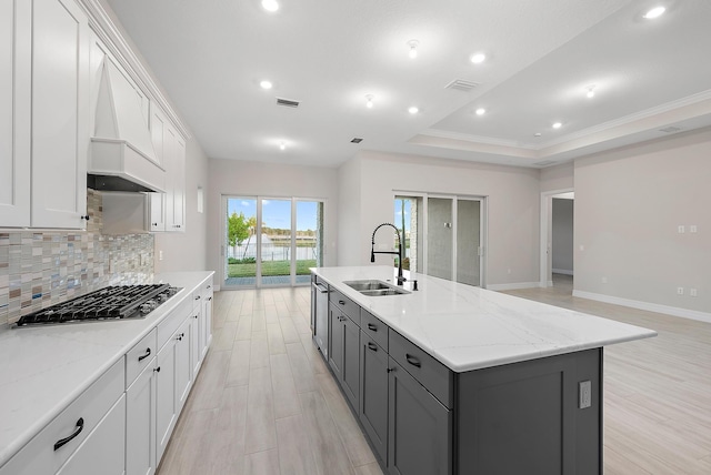 kitchen featuring stainless steel gas stovetop, a center island with sink, sink, light stone counters, and white cabinetry