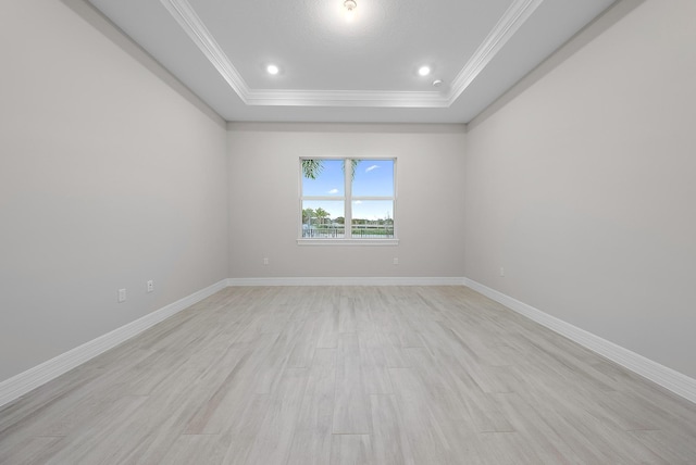 empty room featuring light wood-type flooring, a tray ceiling, and ornamental molding