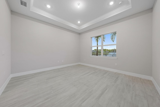 empty room with a raised ceiling, ornamental molding, and light wood-type flooring