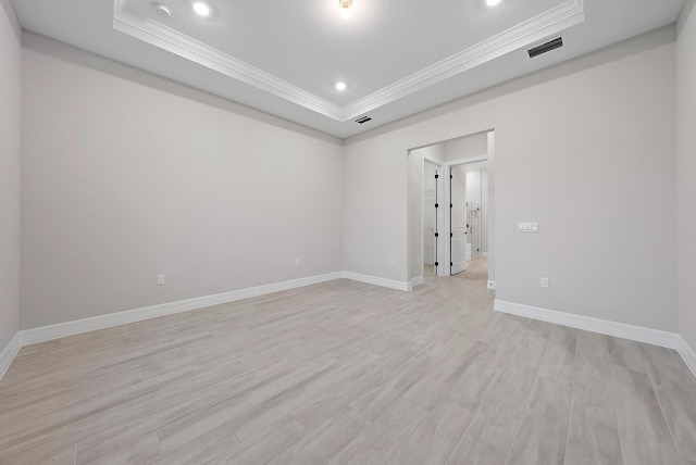 empty room featuring a tray ceiling, crown molding, and light wood-type flooring