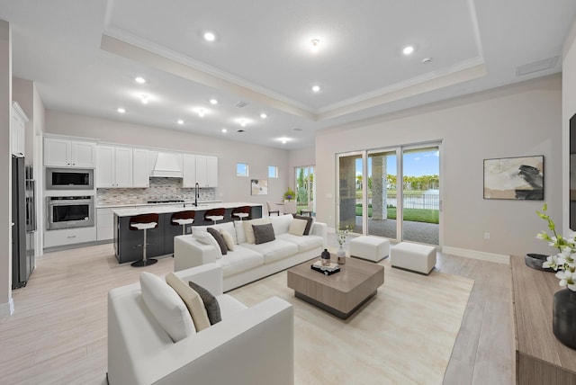 living room with a tray ceiling, ornamental molding, and light wood-type flooring