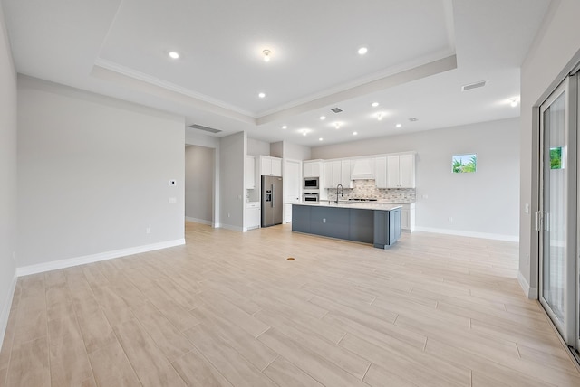 kitchen featuring a center island with sink, a raised ceiling, light wood-type flooring, white cabinetry, and stainless steel appliances