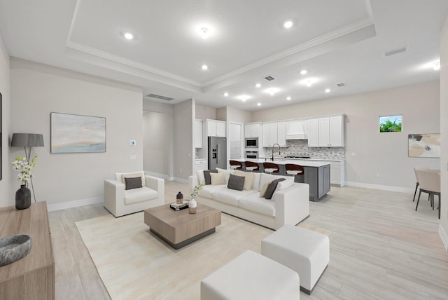 living room featuring light wood-type flooring, a raised ceiling, crown molding, and sink