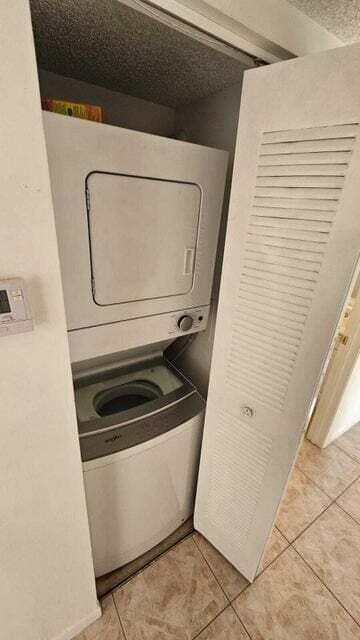 laundry area with a textured ceiling, light tile patterned floors, and stacked washer / dryer