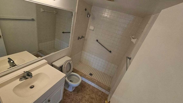 bathroom featuring tile patterned flooring, a tile shower, vanity, and toilet