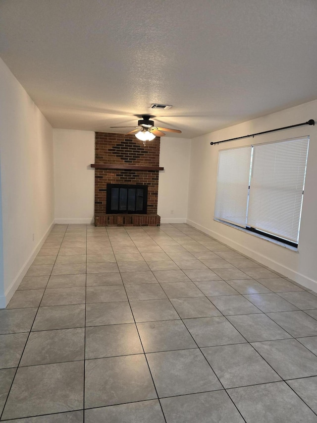 unfurnished living room with a textured ceiling, ceiling fan, light tile patterned floors, and a fireplace