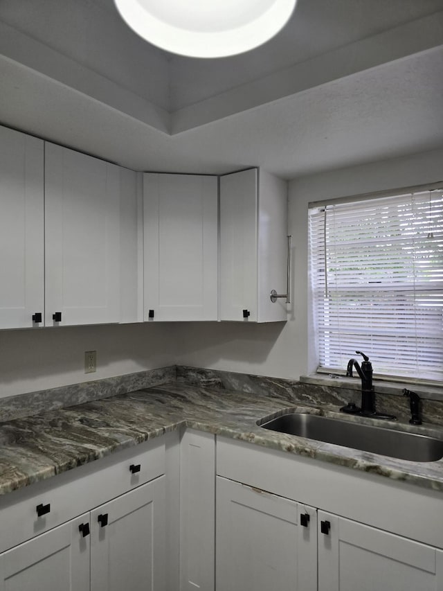 kitchen with a raised ceiling, white cabinetry, sink, and dark stone counters