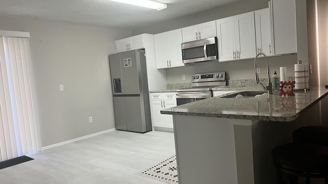 kitchen with sink, kitchen peninsula, dark stone countertops, white cabinets, and appliances with stainless steel finishes