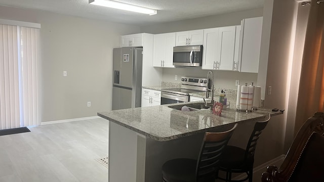 kitchen with white cabinetry, kitchen peninsula, a textured ceiling, a breakfast bar, and appliances with stainless steel finishes