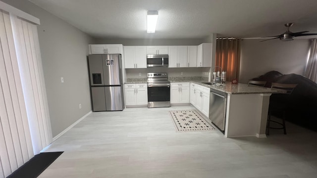 kitchen featuring white cabinetry, sink, kitchen peninsula, dark stone countertops, and appliances with stainless steel finishes