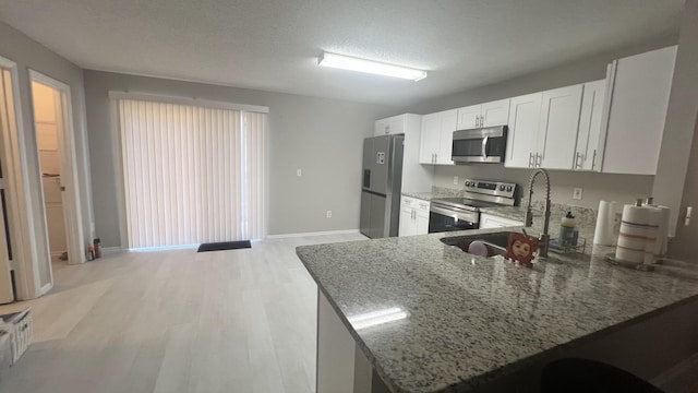 kitchen with kitchen peninsula, white cabinetry, stone countertops, and appliances with stainless steel finishes