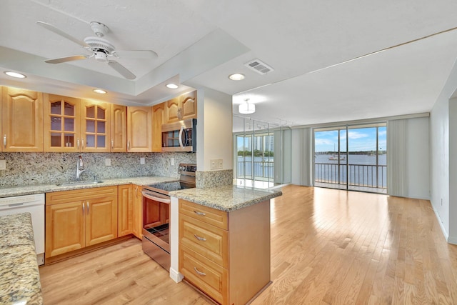 kitchen with a water view, sink, decorative backsplash, appliances with stainless steel finishes, and light hardwood / wood-style floors