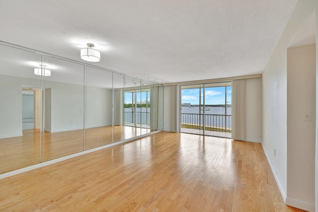 empty room with light hardwood / wood-style flooring, a water view, a textured ceiling, and a wall of windows