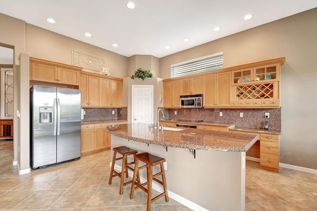 kitchen with sink, appliances with stainless steel finishes, a kitchen breakfast bar, light stone counters, and an island with sink