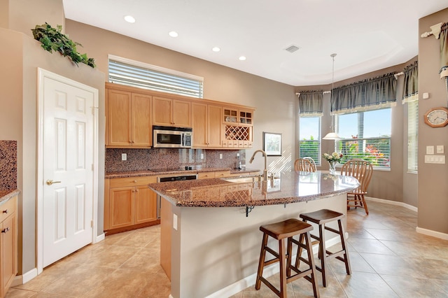 kitchen featuring sink, tasteful backsplash, a center island with sink, hanging light fixtures, and stone counters