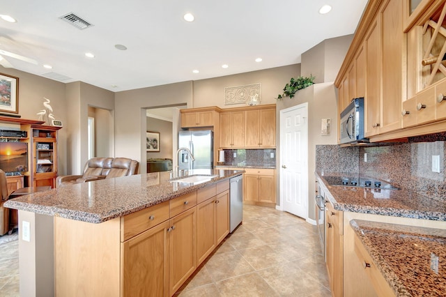 kitchen featuring light stone countertops, sink, light brown cabinetry, a center island with sink, and appliances with stainless steel finishes