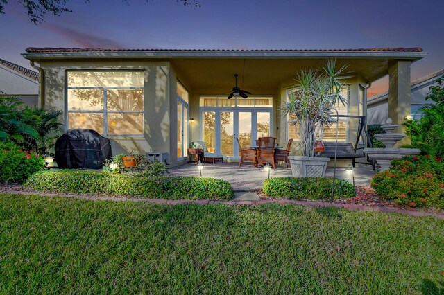 back house at dusk featuring a lawn, a patio, ceiling fan, and french doors