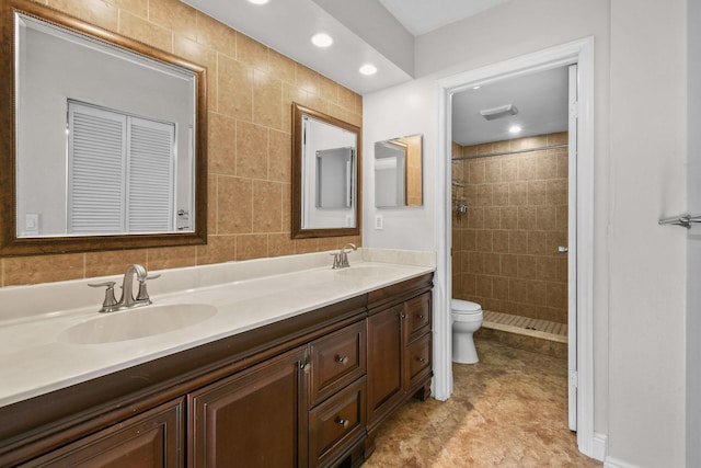 bathroom featuring a tile shower, vanity, toilet, and tile walls