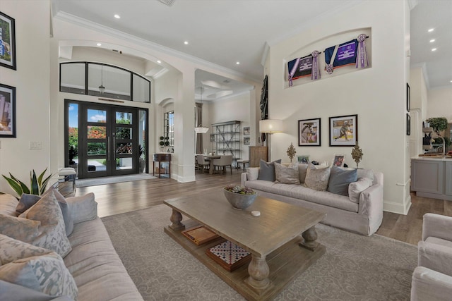 living room with french doors, a towering ceiling, wood-type flooring, and ornamental molding