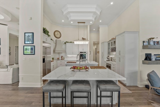 kitchen featuring light stone counters, a center island with sink, white cabinets, and crown molding