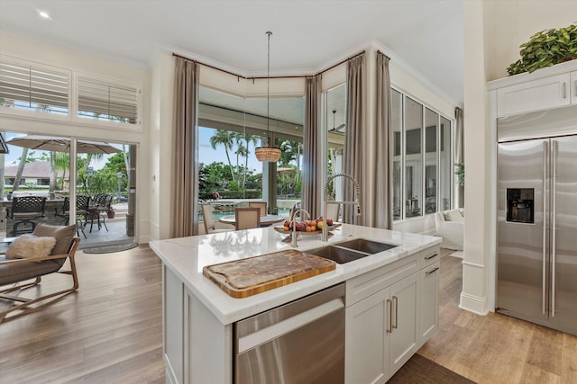 kitchen featuring white cabinetry, sink, stainless steel appliances, an island with sink, and decorative light fixtures