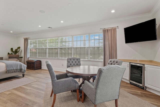 dining area with light wood-type flooring, crown molding, wine cooler, and indoor bar