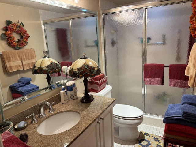 bathroom featuring tile patterned flooring, vanity, toilet, and a shower with door