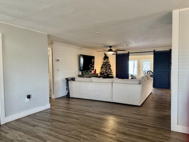 unfurnished living room with a textured wall, dark wood finished floors, a textured ceiling, and a barn door