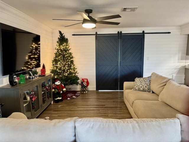 living room featuring ceiling fan, a barn door, wood finished floors, and visible vents