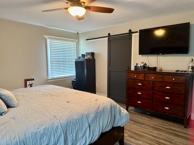 bedroom with a ceiling fan, light wood-type flooring, and a barn door