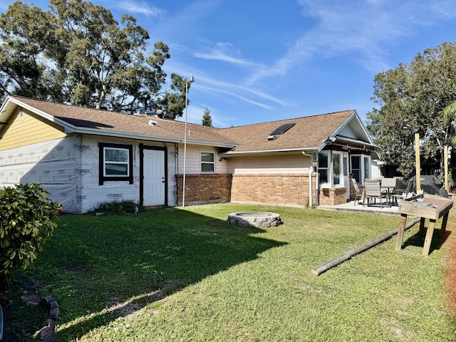 rear view of property with an outdoor fire pit, a patio, roof with shingles, a yard, and brick siding