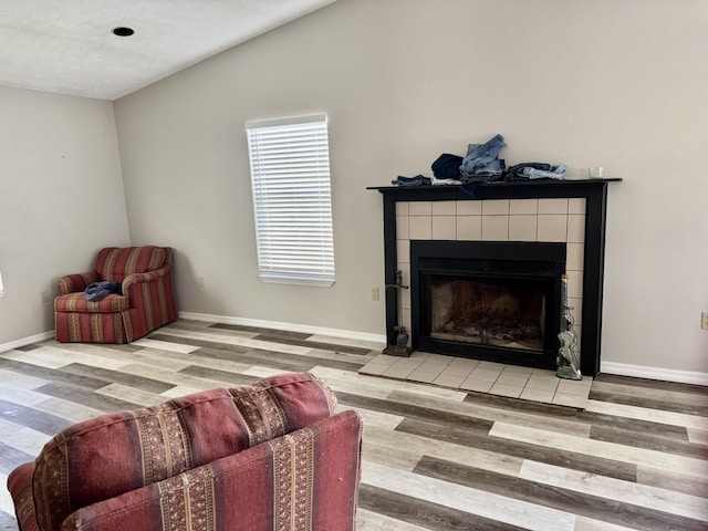 living area with lofted ceiling, a fireplace, baseboards, and wood finished floors